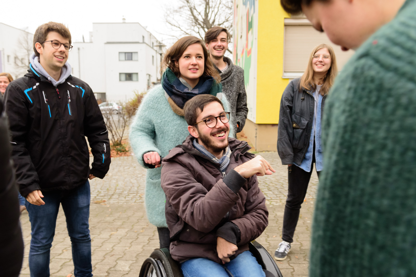 Fünf lächelnde Personen die draußen stehen sind abgebildet. Eine von ihnen sitzt im Rollstuhl und gestikuliert und wir von einer anderen Person geschoben. ©Servicestelle Jugendbeteiligung 2022